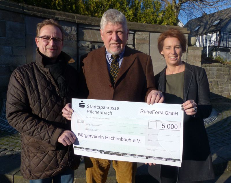 v.l.: Hans-Peter Hasenstab, Jost Arnold und Nina Ehrler bei der Scheckübergabe vor dem Brunnen in Hilchenbach, der mit seinen zwölf Wasserstrahlen sinnbildlich für die zwölf Stadtteile steht. (Foto: Stadt Hilchenbach)
