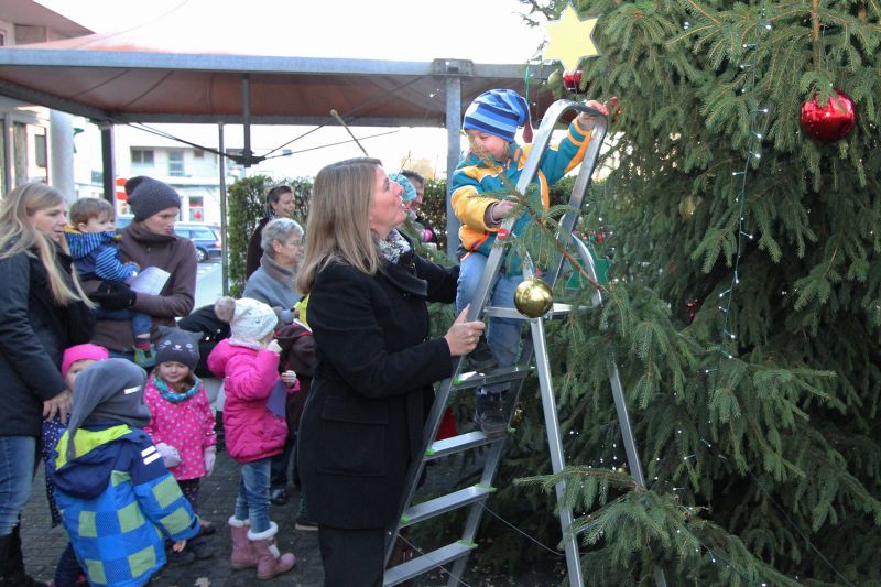 Wilnsdorfs Bürgermeisterin leistete Sicherungsarbeit, während ein Knirps aus dem „Spatzennest“ den Wilnsdorfer Weihnachtsbaum dekorierte. (Foto: Gemeinde Wilnsdorf)